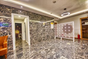 Un vestíbulo con suelo de mármol, mostrador de recepción, un panel decorativo blanco y un extintor.