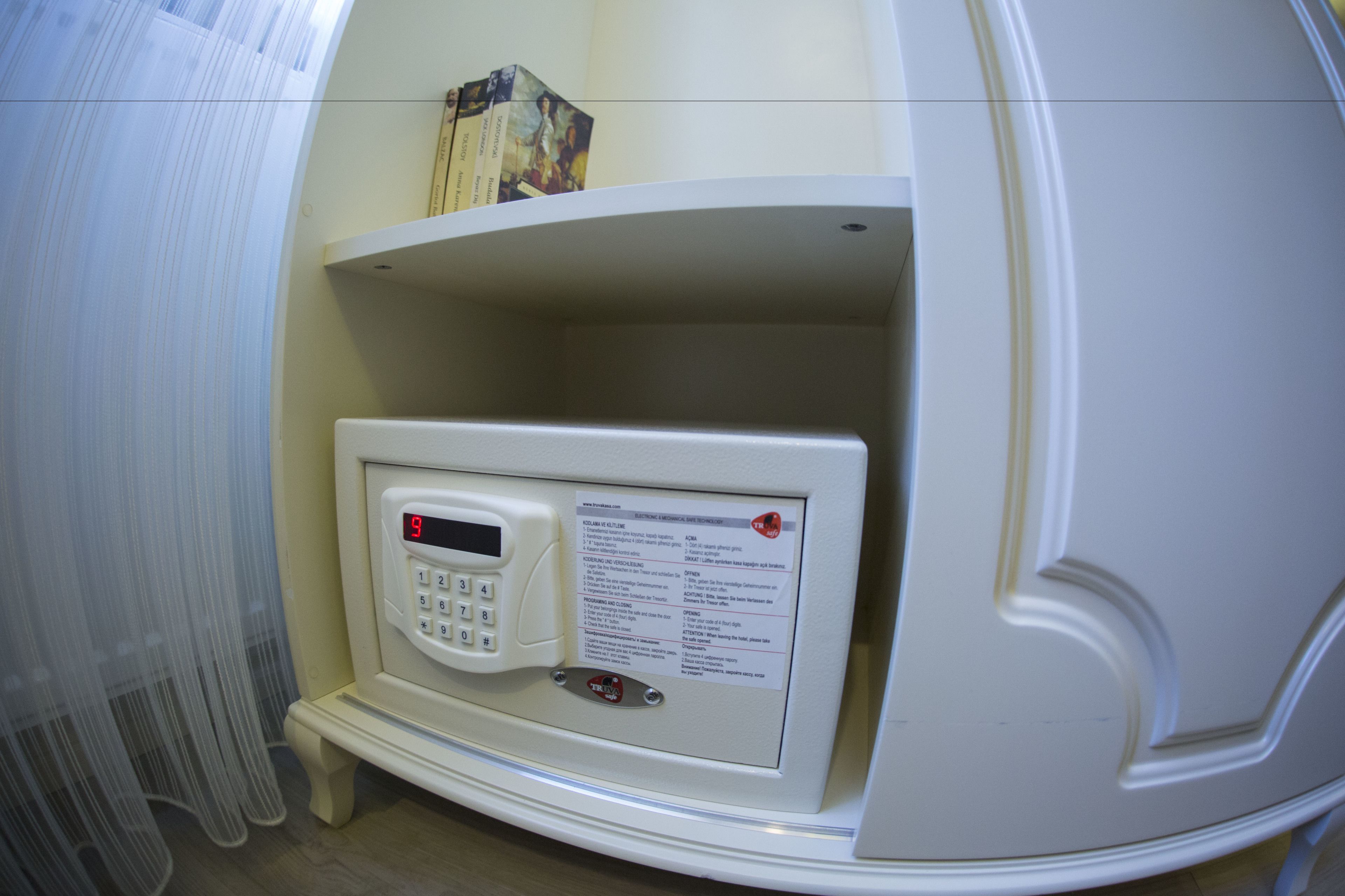 A room with a white wall, a small shelf with books, and a control panel with a digital display.