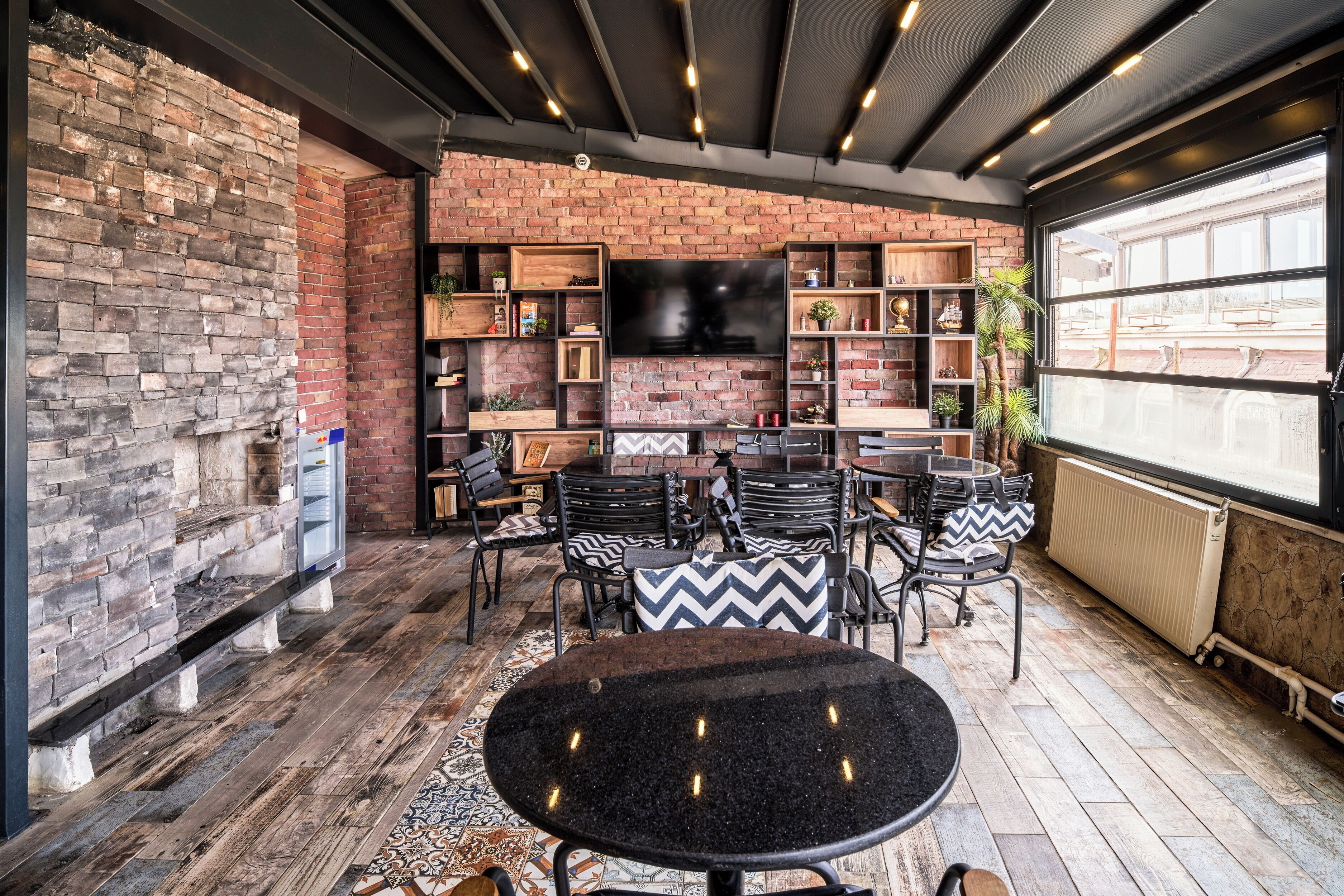 A cozy indoor seating area with brick walls, a flat-screen TV, and a mix of wooden and metal furniture.