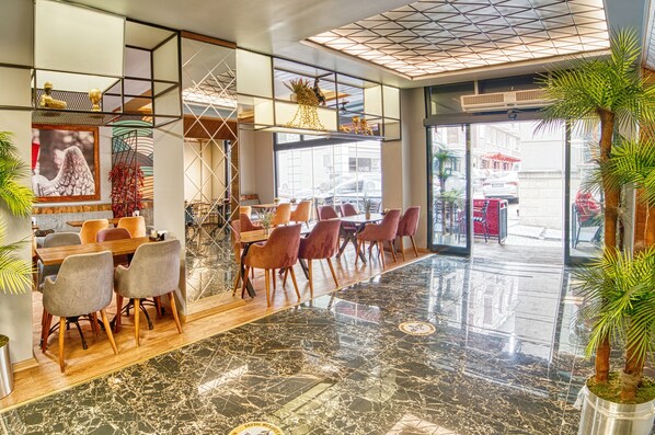 Un hall d’hôtel moderne avec une longue table à manger, des sièges confortables et une grande fenêtre donnant sur la rue.