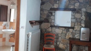 A bathroom with a stone wall, a white radiator, a wooden chair, a small shelf, and a white sink. - B&B Gennargentu (Fonni)