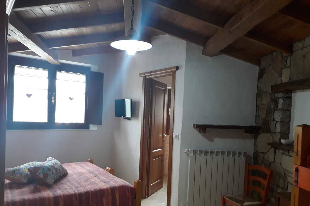 A bedroom with a bed, a chair, a radiator, and a stone wall.