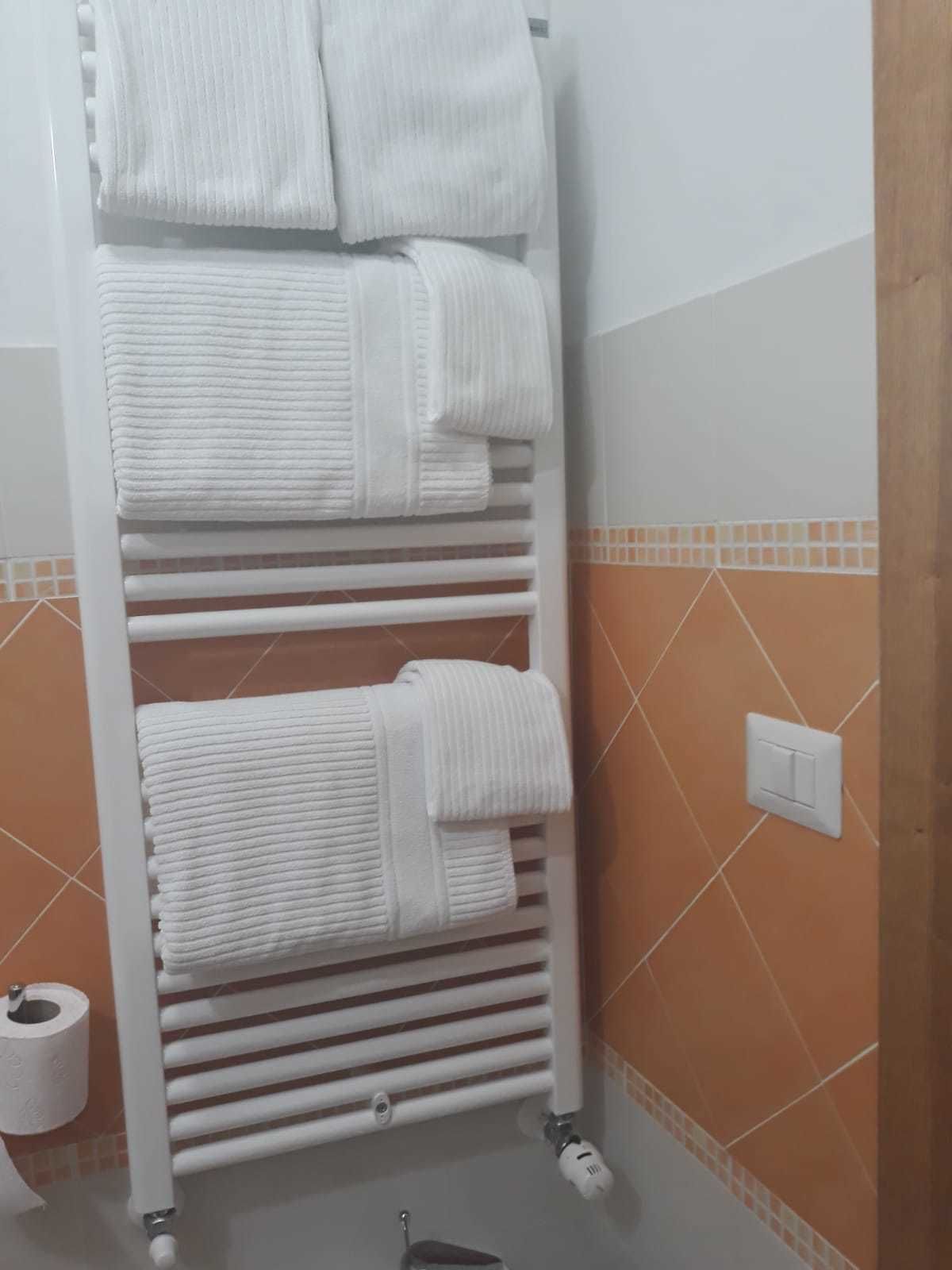Un porte-serviettes blanc, sur lequel sont disposés plusieurs serviettes, dans une salle de bain dont les murs sont recouverts de carreaux orange et blancs.