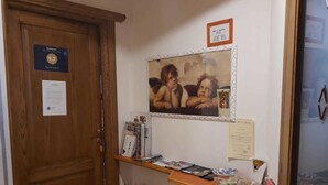 A hotel reception area with a wooden door, a framed picture on the wall, a shelf with magazines and toiletries, and a sign indicating the room rate. - B&B Gennargentu (Fonni)