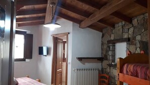 A bedroom with a wooden ceiling, a stone wall, a bed, a chair, and a television. - B&B Gennargentu (Fonni)