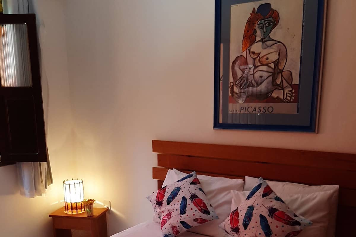 A neatly made bed with white linens, two pillows with a feather pattern, and a framed artwork on the wall.