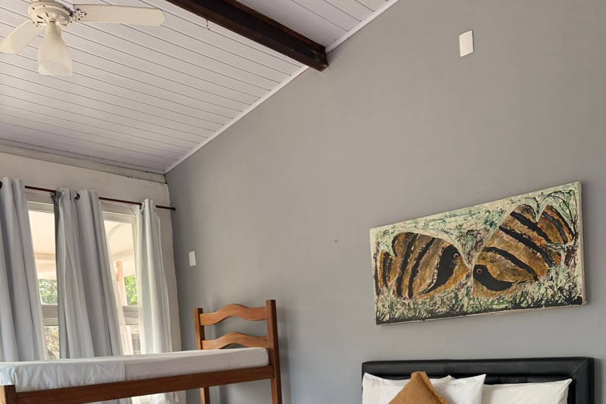 A bedroom with a bunk bed, a single bed, a ceiling fan, a painting, and a window with curtains.