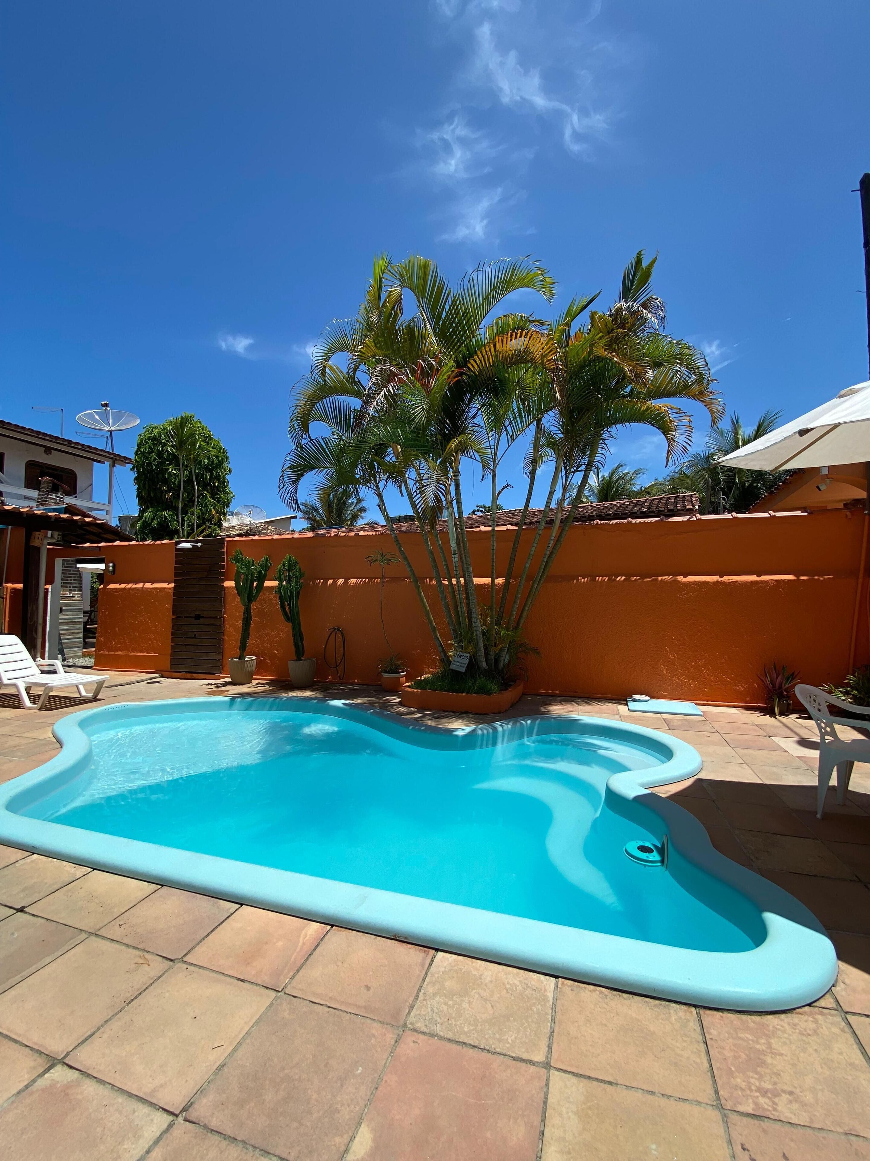 A swimming pool with a tiled deck, surrounded by a low orange wall and palm trees.