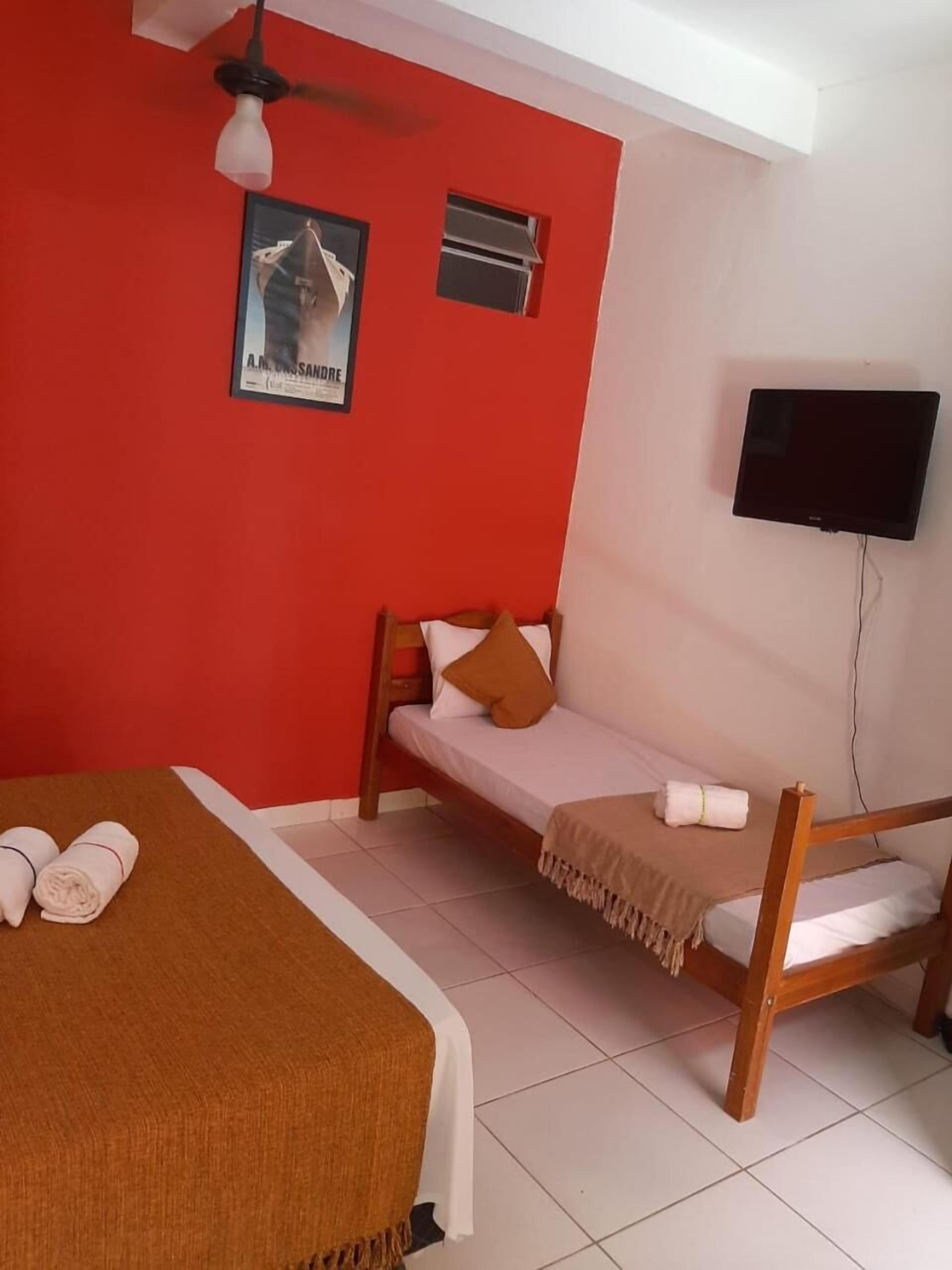 A room with a bed, a small sofa, a ceiling fan, a TV, and a poster on the wall.