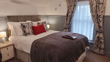 A neatly made bed with a red pillow, a bedside lamp, and a book on the bed.