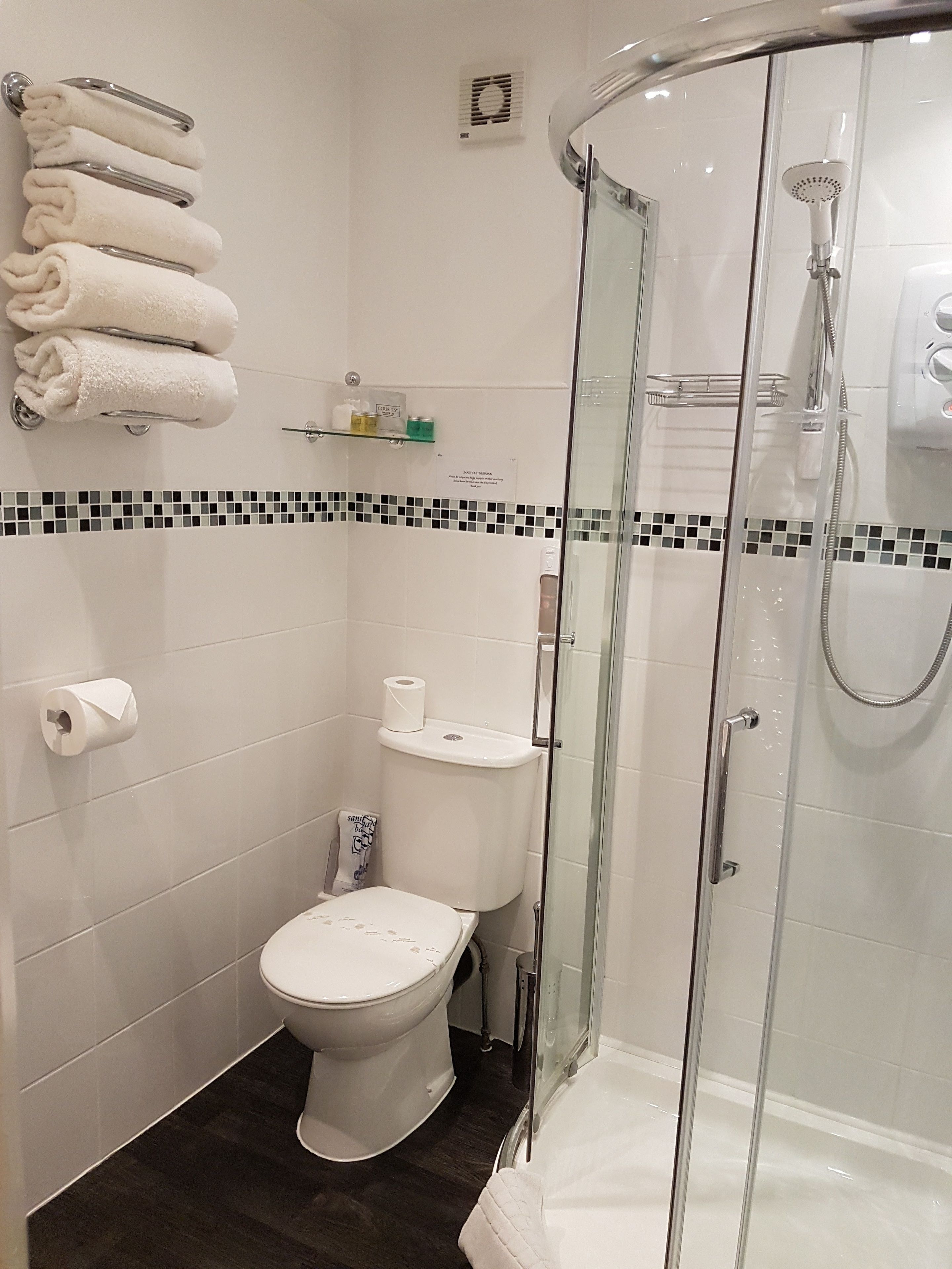 A modern bathroom with a glass-enclosed shower, a toilet, and a towel rack with neatly folded towels.