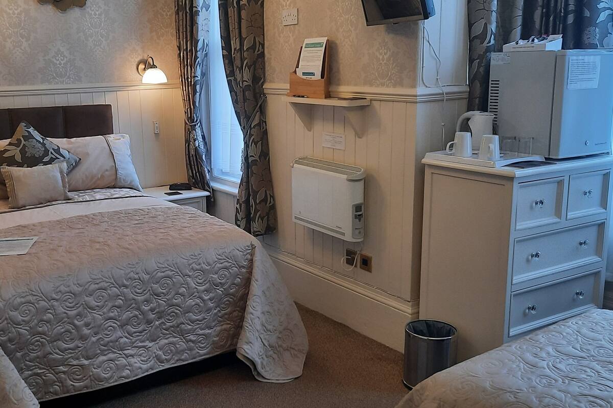 A hotel room with a large bed, bedside tables, a dresser, a radiator, and a television.