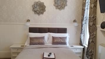 A neatly arranged bedroom with a large bed, bedside tables, a chandelier, and decorative wall pieces.
