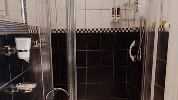 Un baño moderno con ducha de vidrio, un lavamanos blanco y grifería cromada, y un salpicadero de azulejos blanco y negro.