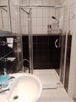 Un baño moderno con ducha de vidrio, un lavamanos blanco y grifería cromada, y un salpicadero de azulejos blanco y negro.