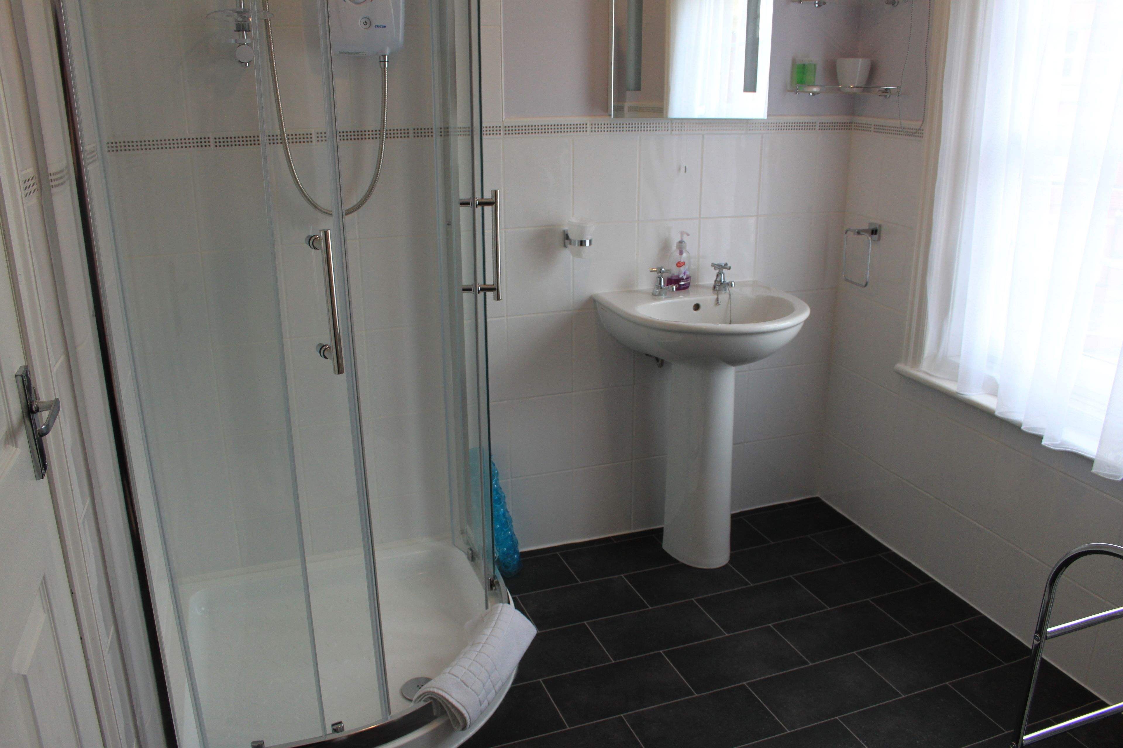Une salle de bain avec une douche à parois de verre, un lavabo blanc et une fenêtre avec des rideaux.