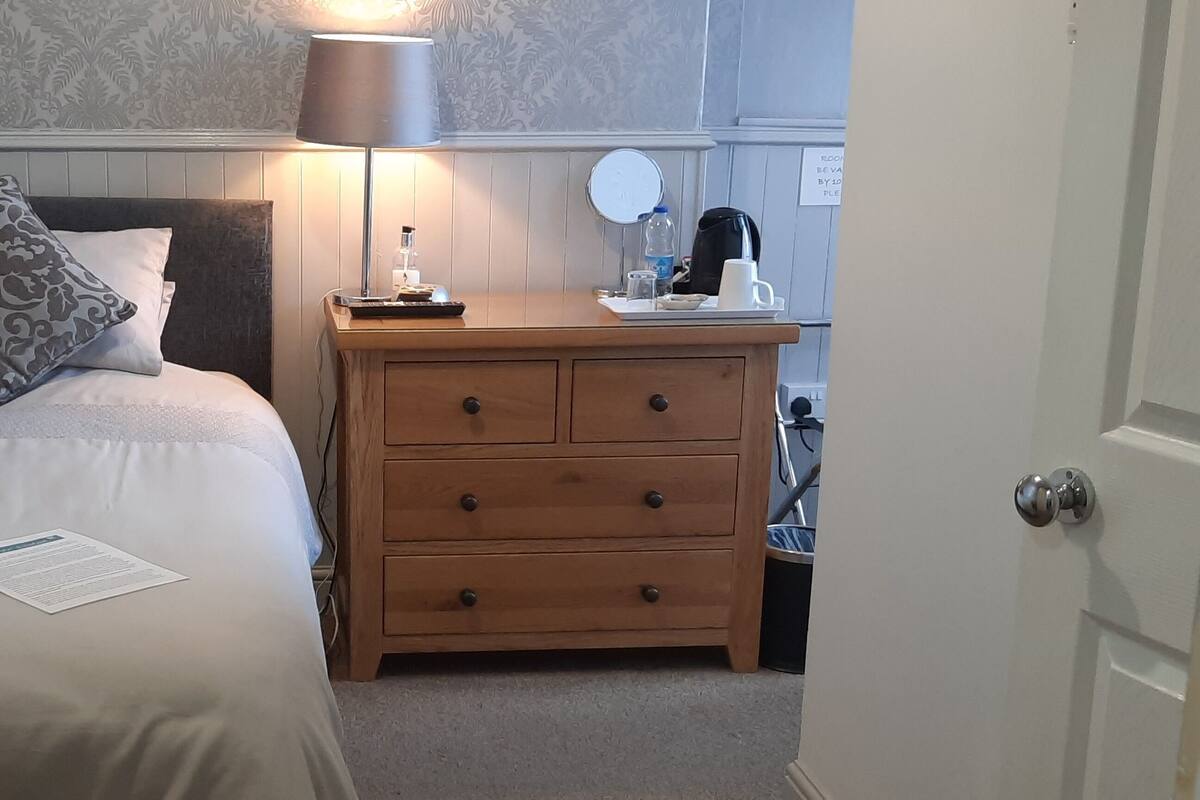 A neatly made bed with a pillow, a bedside table with a lamp, and a small mirror.