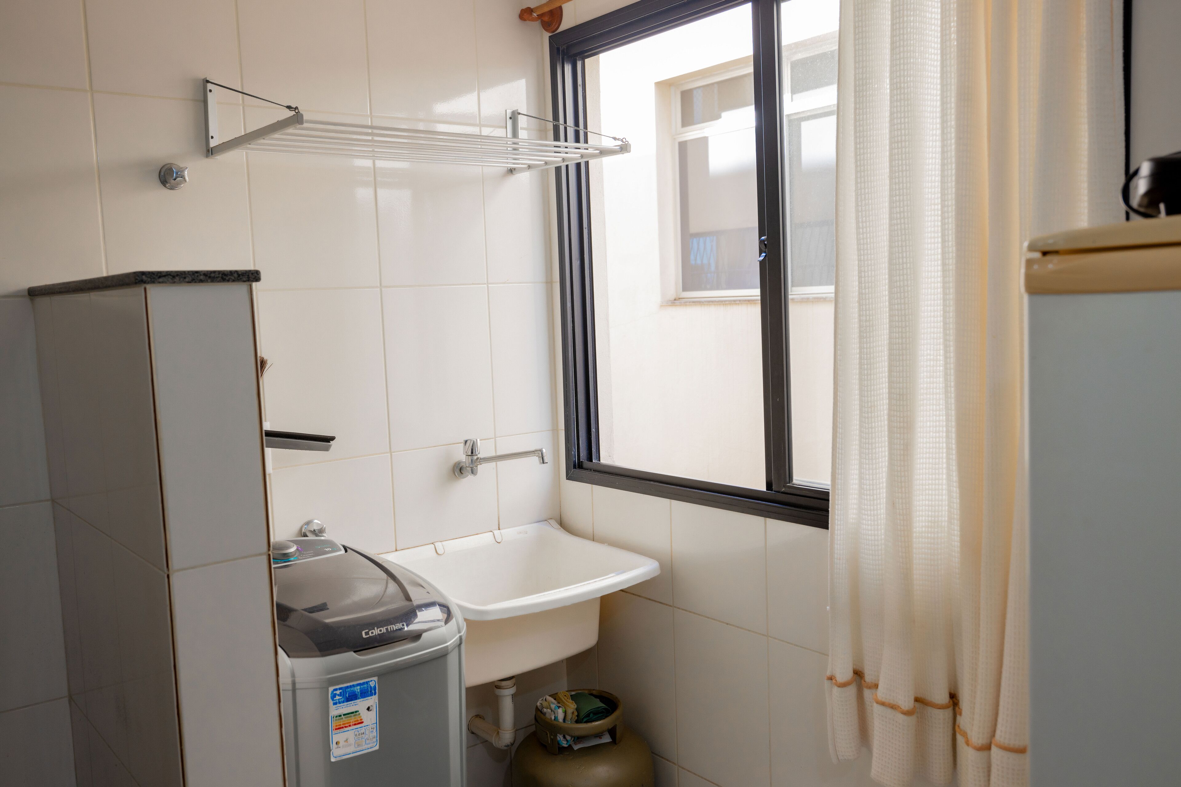 A bathroom with a sink, a window with a view, a gas cylinder, and a trash bin.