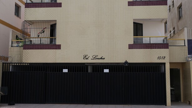 A building facade with a tiled wall, balconies, and a gated entrance. - Edifício Londres (Guarapari)