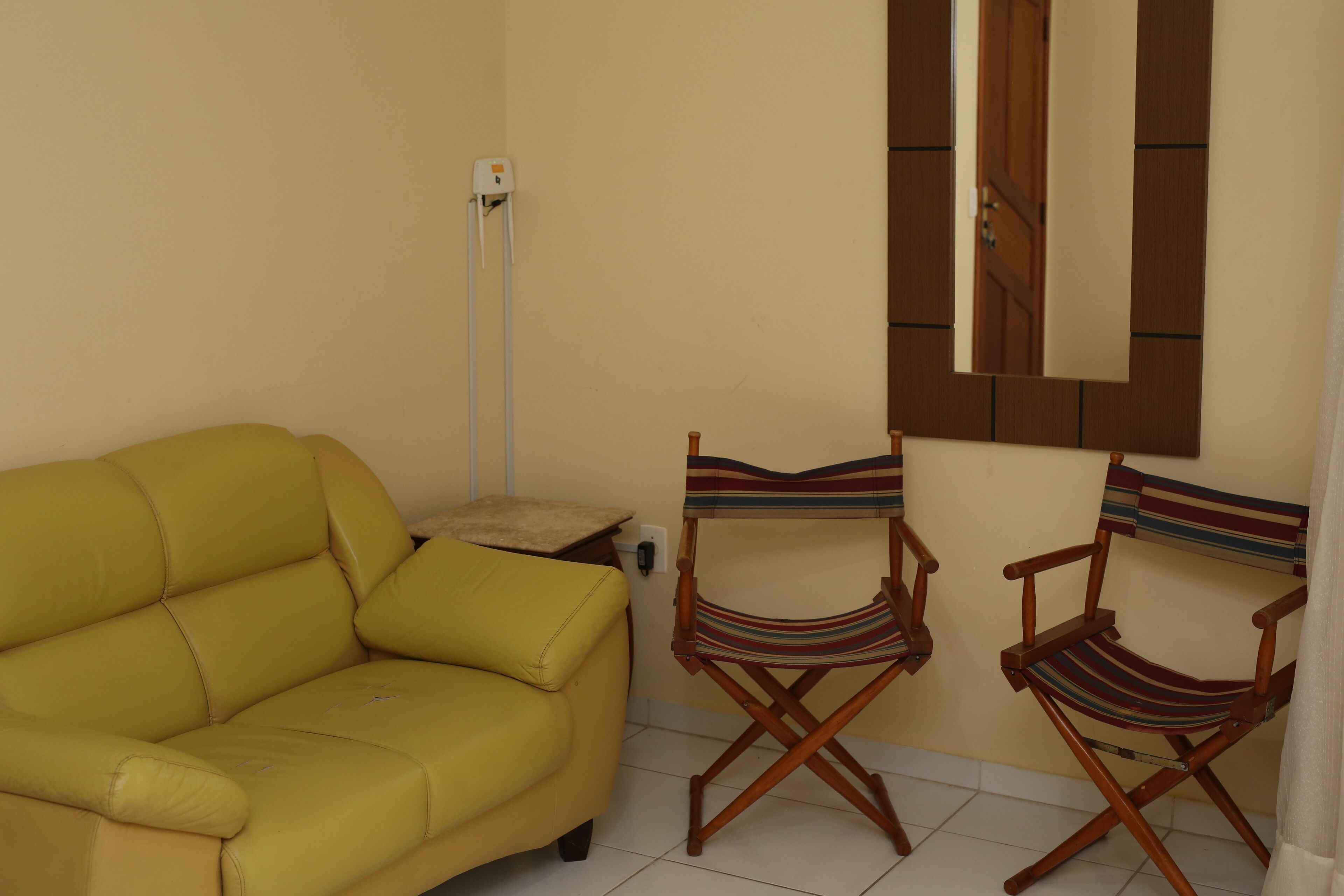 Un sofá amarillo, dos sillones a rayas tipo director, un espejo y una mesita con un cojín.