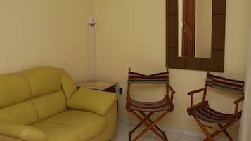 Un sofá amarillo, dos sillones a rayas tipo director, un espejo y una mesita con un cojín.