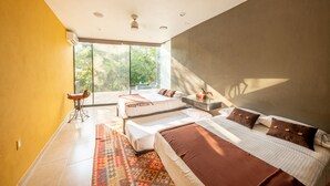 A modern bedroom with a large bed, a sofa, and a view of greenery through the window.