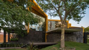 Una casa moderna con un diseño arquitectónico único, que presenta un gran ventanal y un árbol en primer plano.