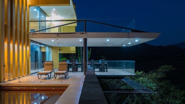 A modern building with a glass facade, outdoor seating area, and a pool.