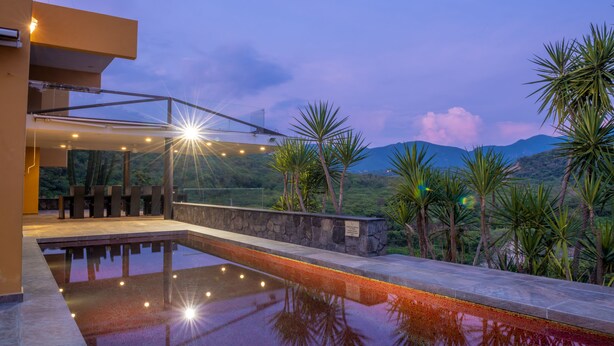 Un área de piscina moderna al aire libre, con una vista despejada del paisaje circundante, que incluye palmeras y montañas a la distancia.