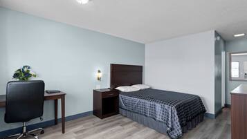 Ein Schlafzimmer mit einem Bett, einem Schreibtisch, einem Stuhl, einem Nachttisch und einer Wandlampe.