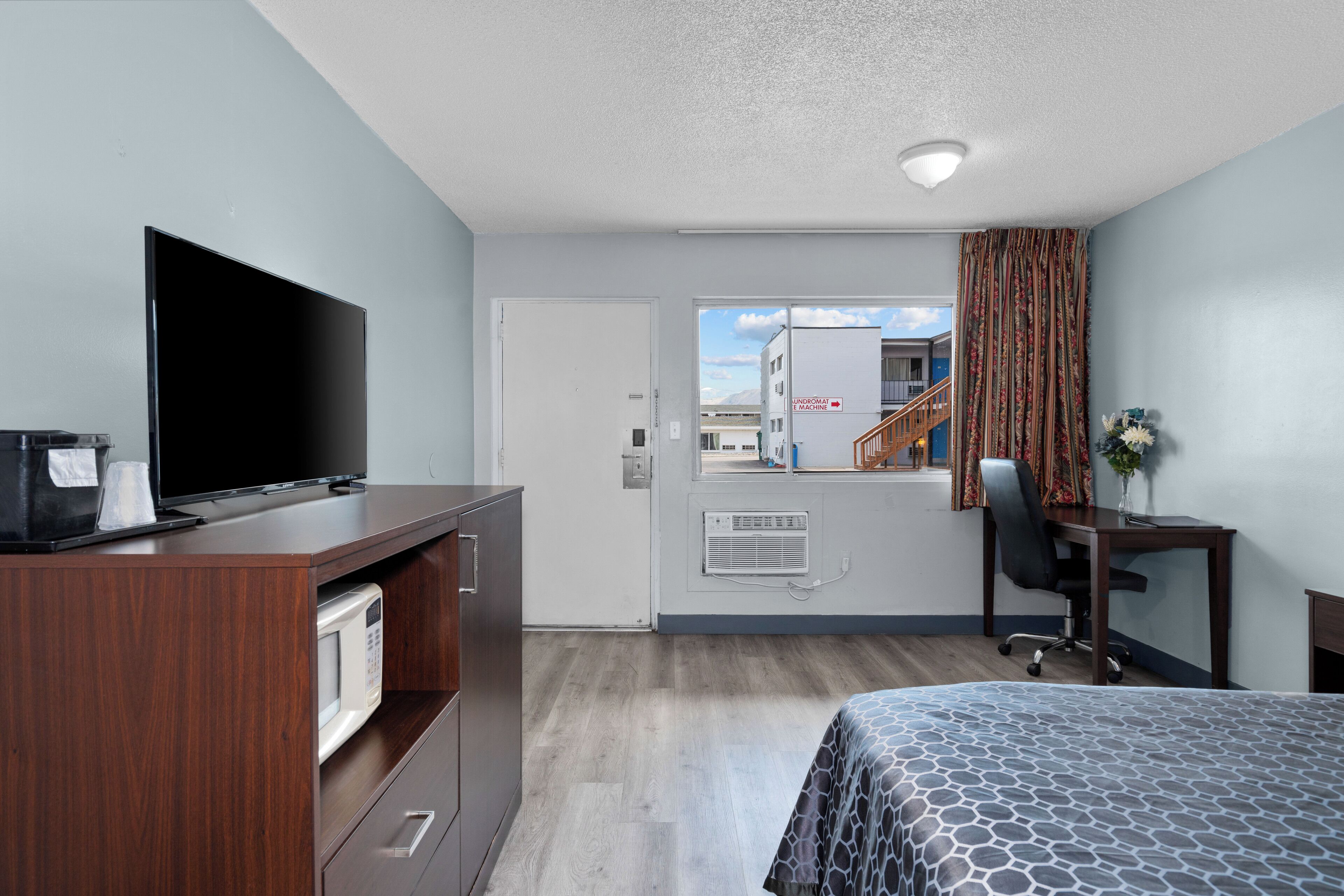Habitación de hotel con cama, escritorio, televisor, microondas y vistas al exterior.