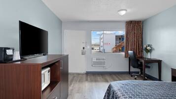 Habitación de hotel con cama, escritorio, televisor, microondas y vistas al exterior.