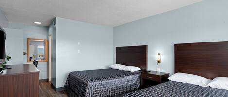 A hotel room with two beds, a desk, and a mirror.