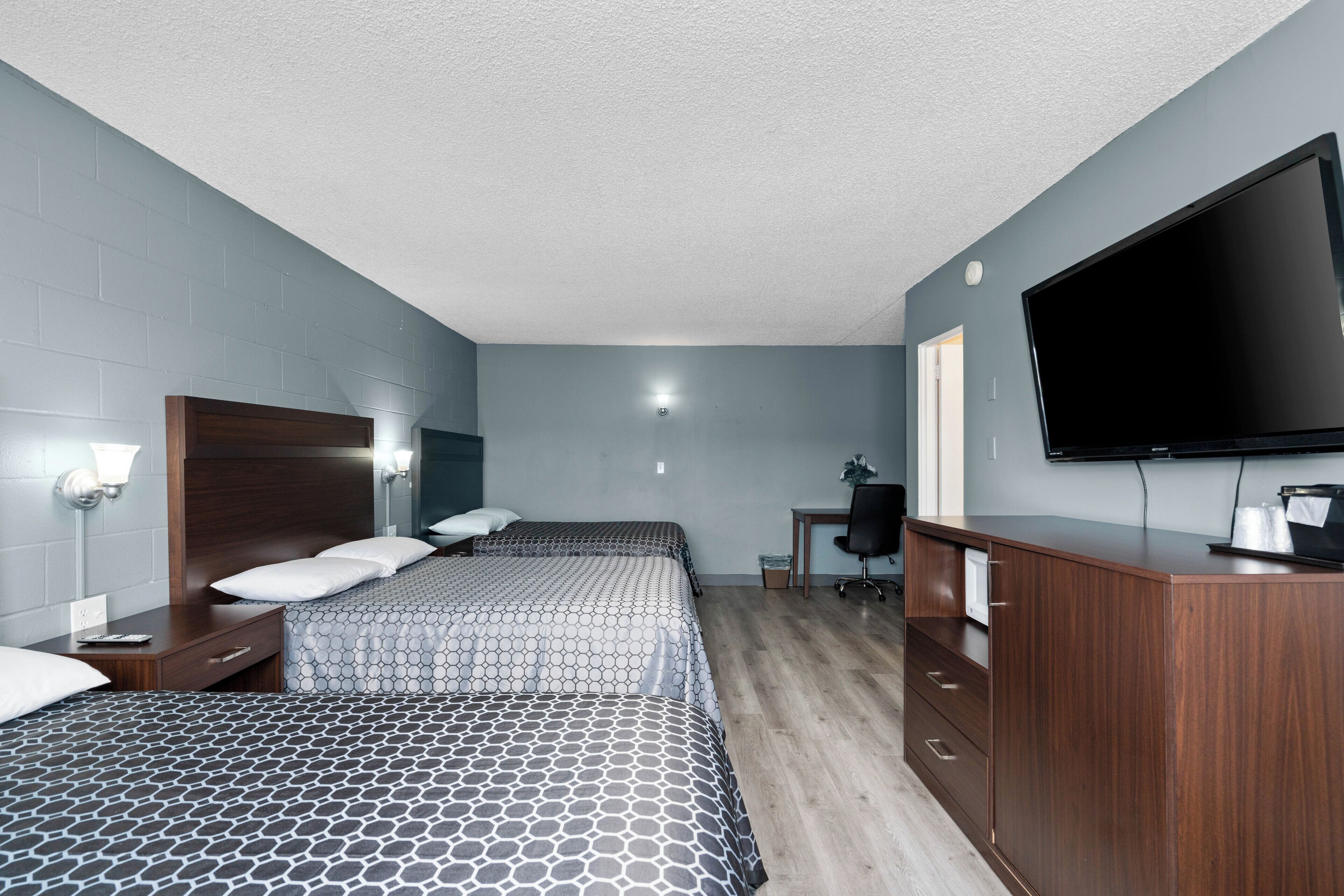 A hotel room with two beds, a desk, a flat-screen TV, and a cabinet.