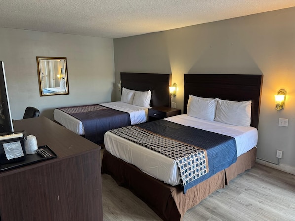 Habitación de hotel con dos camas, un escritorio con computadora y teléfono, y un espejo.