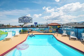 Une piscine avec des chaises longues, un panneau indiquant « Holiday Lodge », et une fresque représentant une scène de plage.