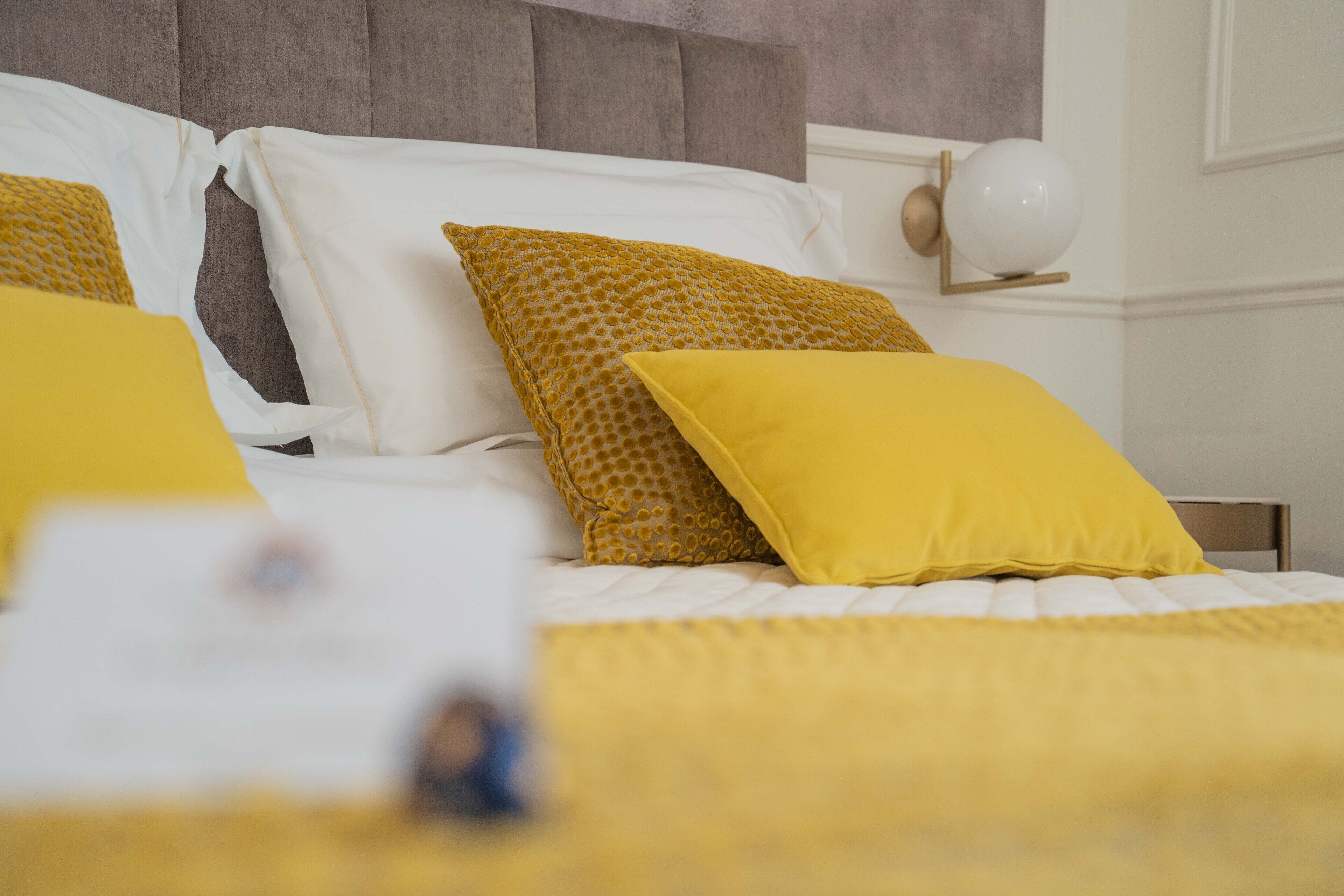 Un letto con biancheria gialla e bianca, una testiera e un comodino con una lampada.