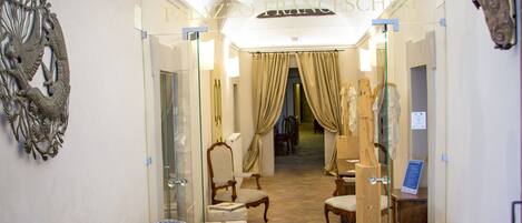 A hallway with wicker chairs, a chandelier, and a carpet with 'Palazzo Franceschini' text.