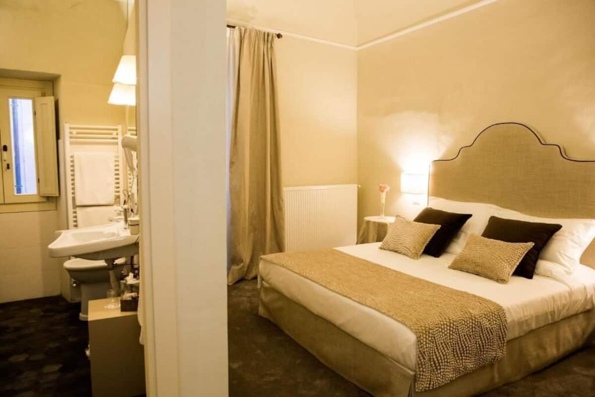 Ein Hotelzimmer mit Bett, Nachttisch, Lampe und einem Badezimmer mit Waschbecken und Toilette.