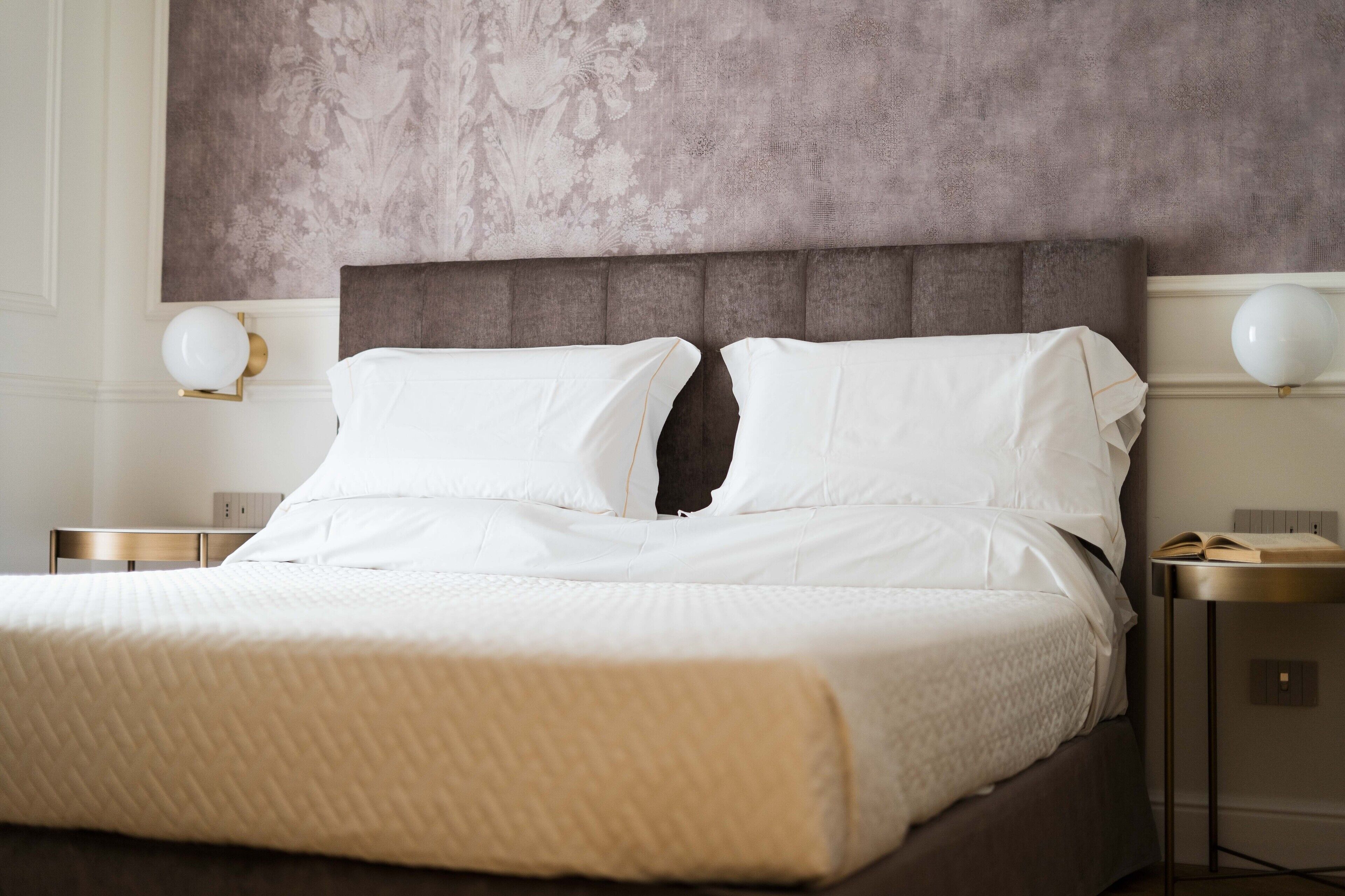 A neatly made bed with white linens, a padded headboard, and two bedside tables with lamps.