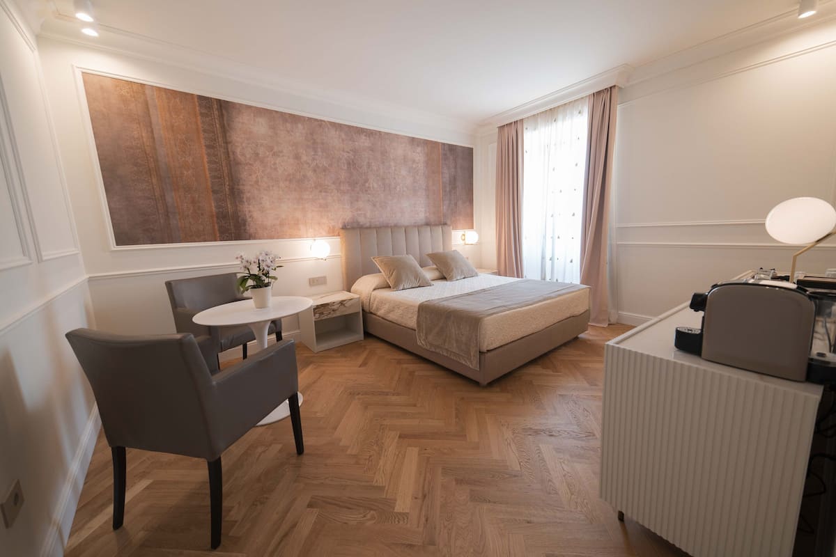 Ein modernes Hotelzimmer mit einem großen Bett, einem Schreibtisch, einem Sessel und einem kleinen Tisch mit Topfpflanze.