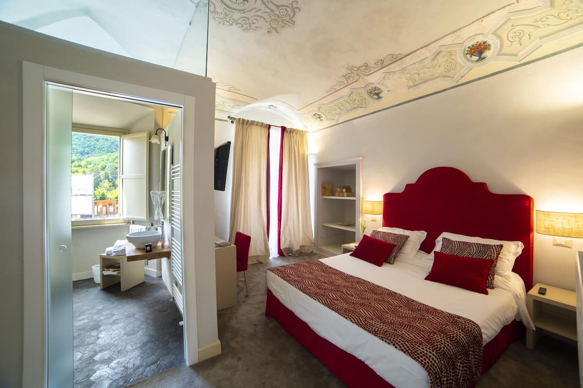 Ein Schlafzimmer mit einem großen Bett, einem Nachttisch, einem Schrank und einem Badezimmer mit Waschbecken und Spiegel.