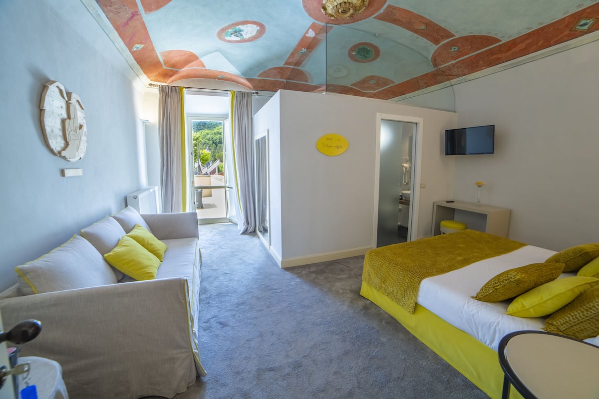 Ein Hotelzimmer mit Bett, einer Couch, einem Fernseher und einer Decke mit einem einzigartigen Design.
