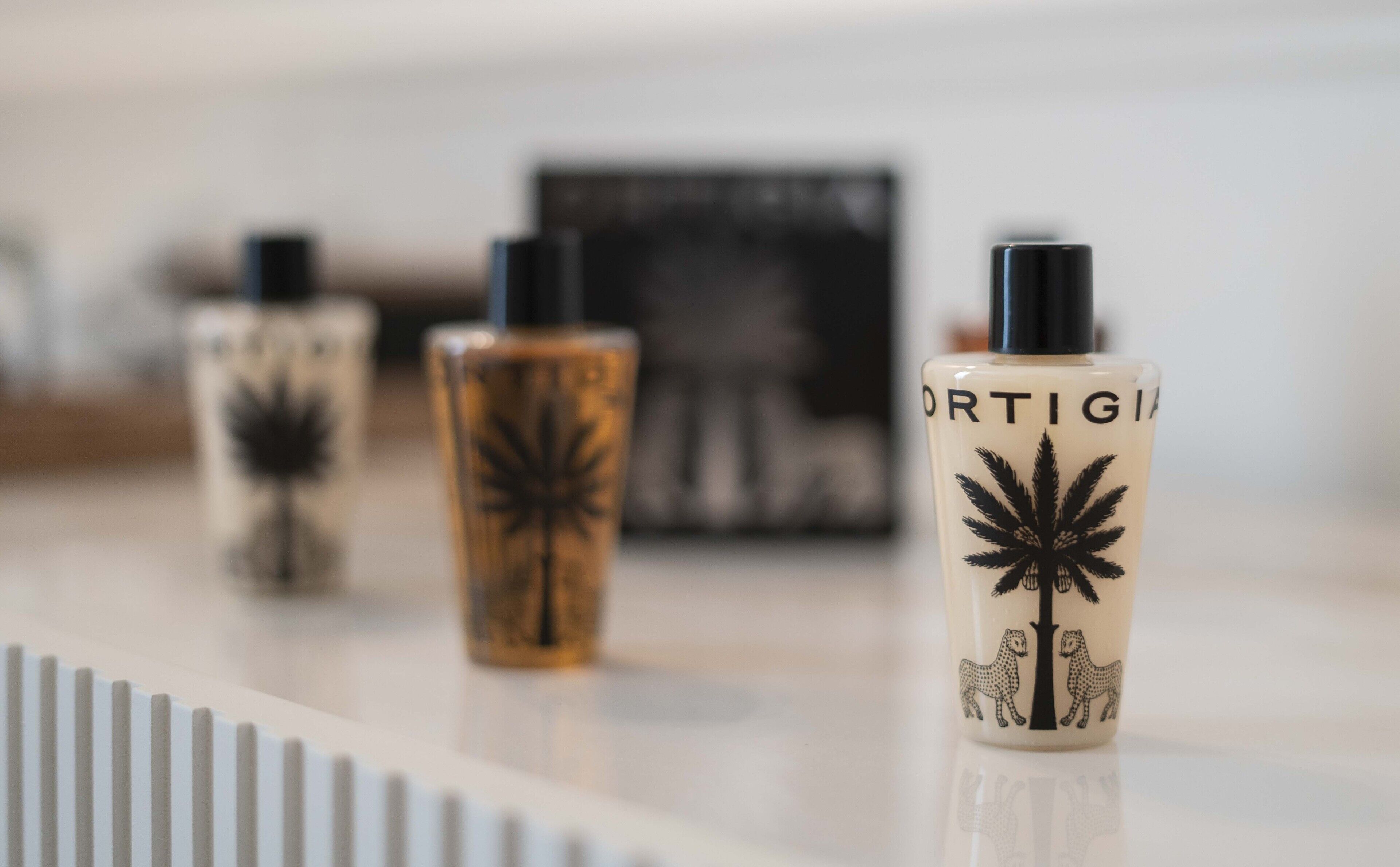 Three bottles of perfume with a tree and leopard design on a reflective surface.