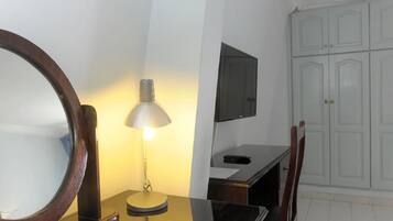 A room with a desk, a round mirror, a lamp, a TV mounted on the wall, and a wardrobe.
