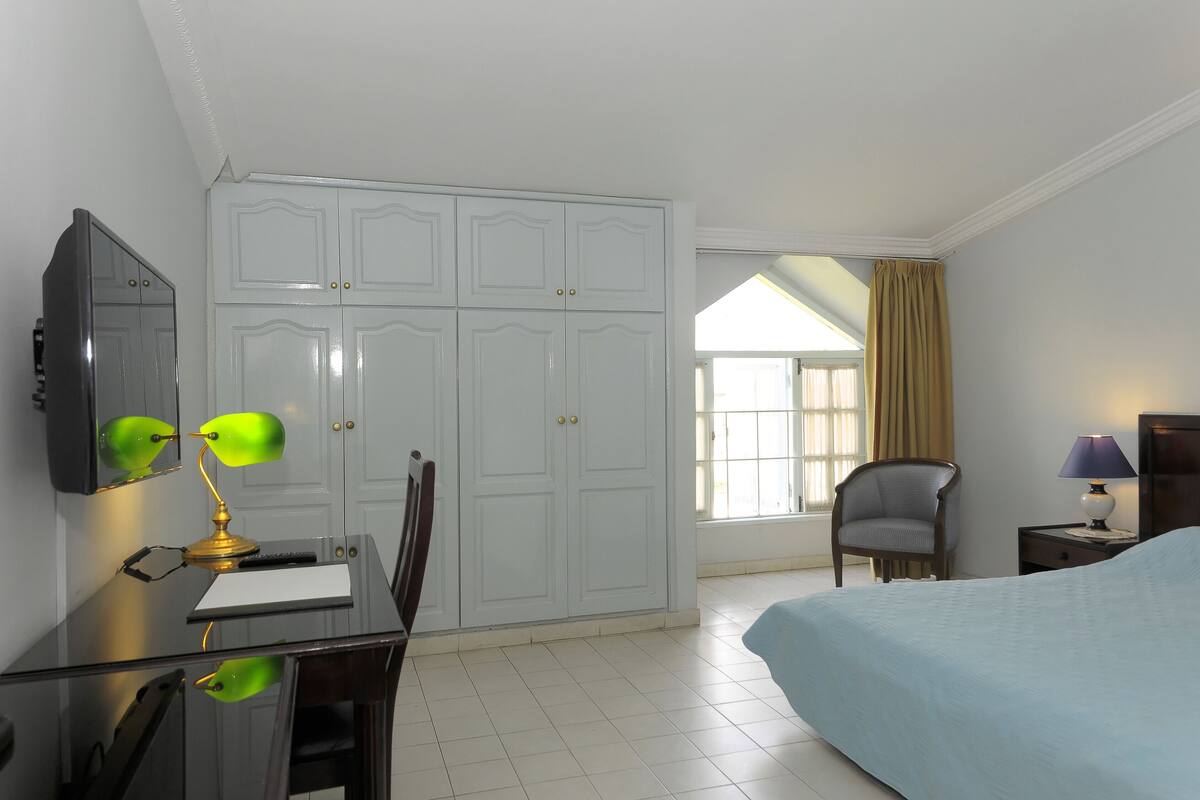 A hotel room with a bed, desk, chair, wardrobe, and a window with curtains.