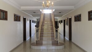 Uma escadaria imponente com um lustre, ladeada por portas e quadros, que dá acesso a um andar superior.
