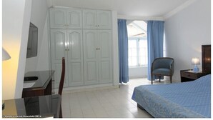 Um quarto com cama, guarda-roupa, cadeira, escrivaninha e janela com cortinas.
