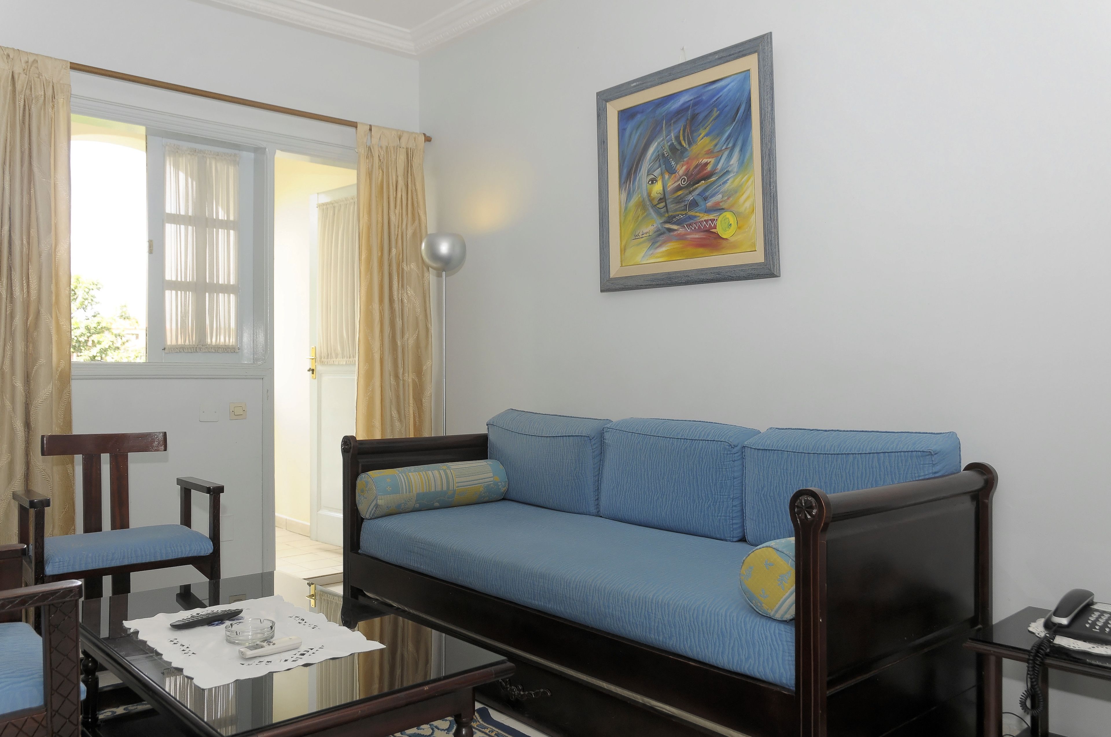 Una sala de estar con un sofá azul, una silla de madera, una mesa de centro de vidrio y un cuadro en la pared.