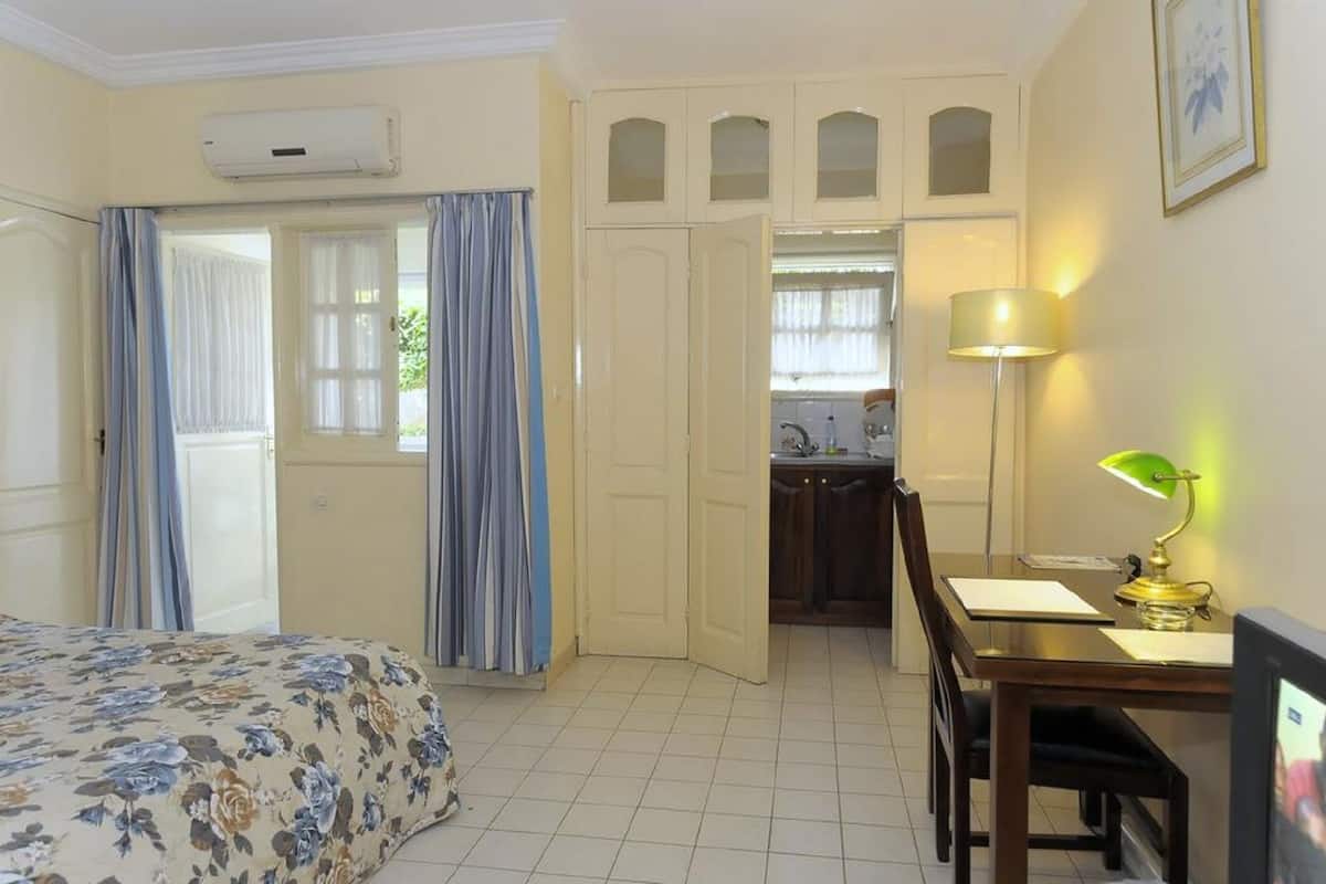 A hotel room with a bed, a desk with a lamp, a television, a kitchen area, and a bathroom.